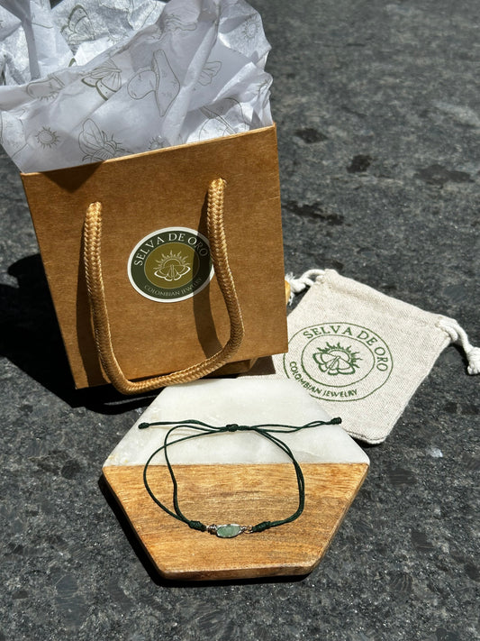 handmade raw emerald bracelet wrapped in silver wire and set on a forest green adjustable cord displayed with selva de oro jewelry packaging