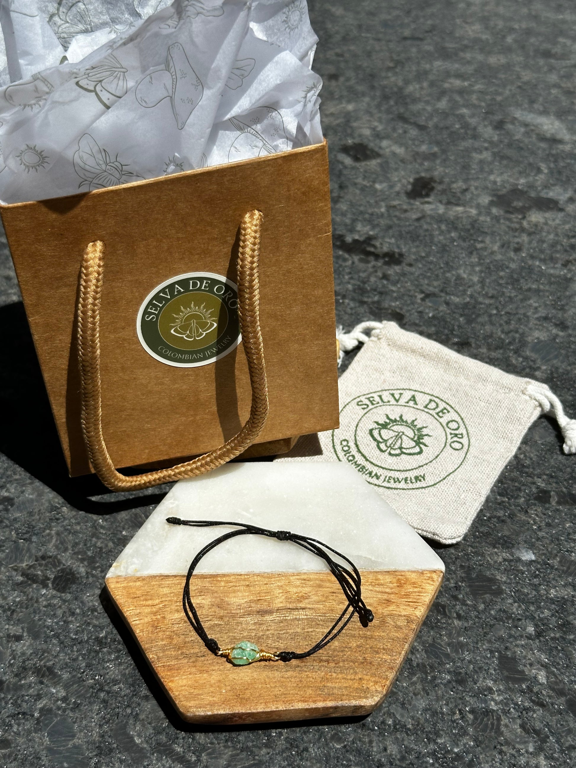 handmade raw emerald bracelet wrapped in gold wire and set on a black adjustable cord displayed with selva de oro jewelry packaging