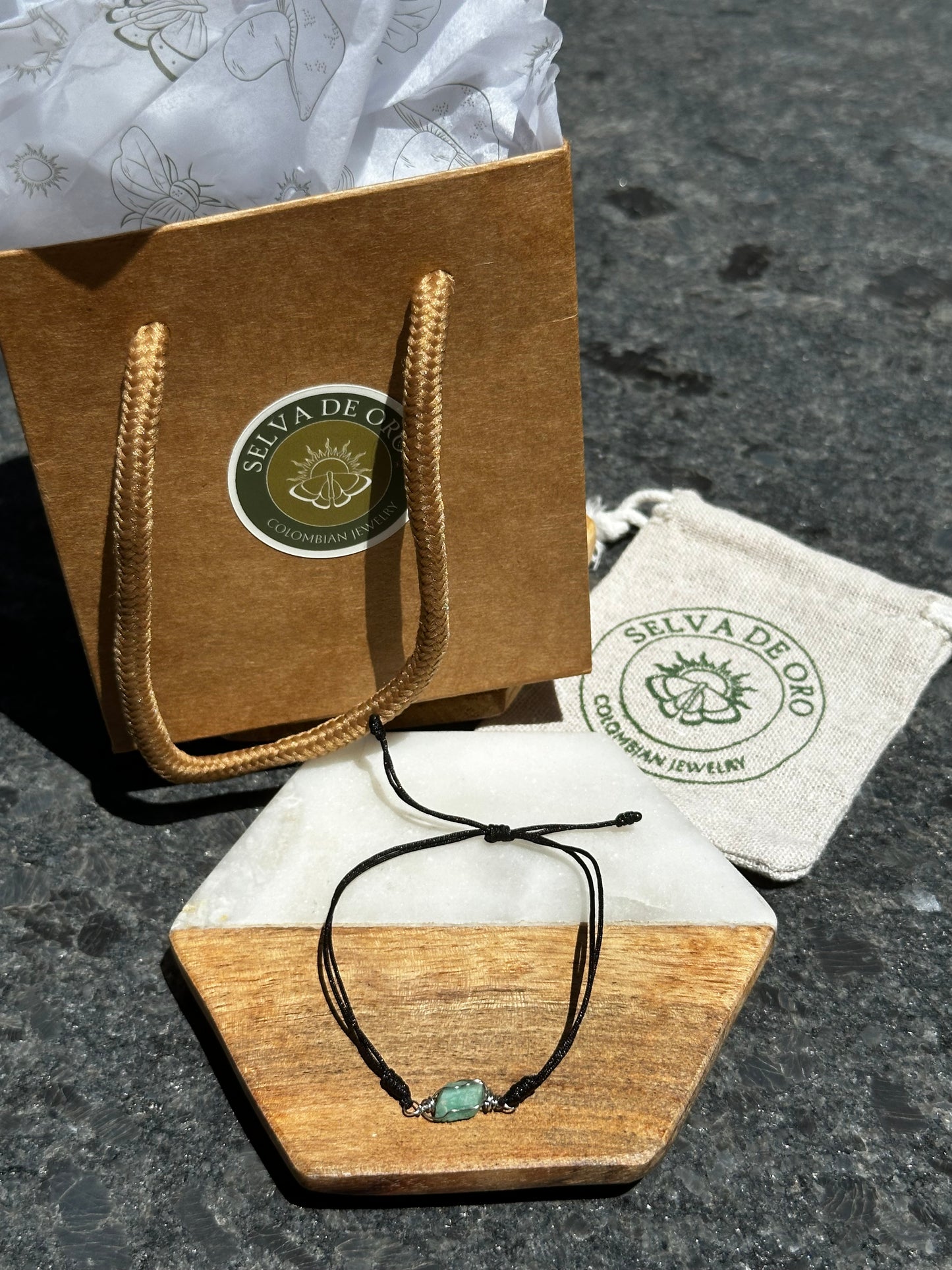 handmade raw emerald bracelet wrapped in silver wire and set on a black adjustable cord displayed with selva de oro jewelry packaging