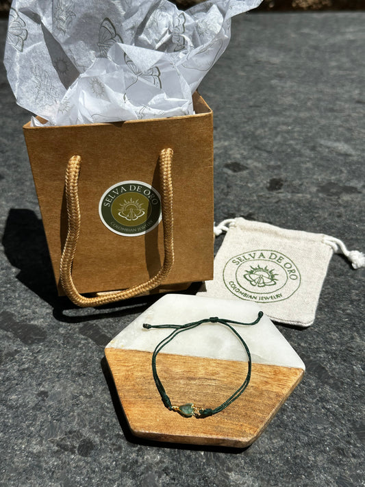 handmade raw emerald bracelet wrapped in gold wire and set on a forest green adjustable cord displayed with selva de oro jewelry packaging